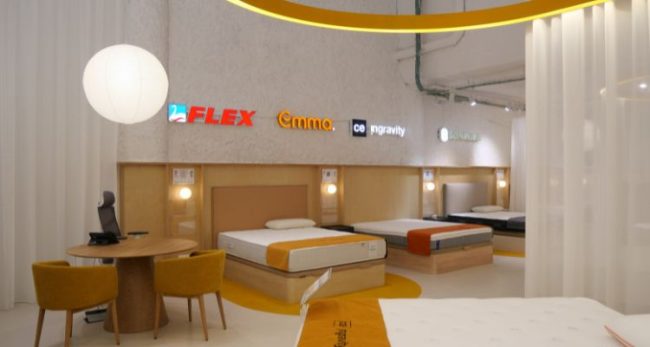 Exposición de colchones en la tienda Colchón Exprés Ribera de Curtidores con logotipos de Flex, Emma, Ingravity y Sonpura en la pared.