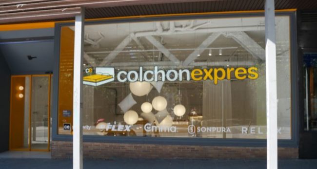 Escaparate de la tienda Colchón Exprés en Ribera de Curtidores, Madrid, con logotipos de Flex, Emma, Sonpura, Ingravity y Relax visibles en el cristal.